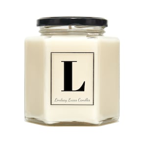 May include: A hexagonal glass jar candle with a black lid. The candle is white and has a black label with the letter "L" and the text "Lindsay Lucas Candles".