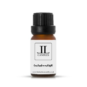 May include: A small brown glass bottle with a black cap. The bottle has a white label with the text "JL CANDLES" and "Car Freshener Refill". The website address "www.lindsaylucascandles.co.uk" is also printed on the label. The bottle is designed for car freshener refills.