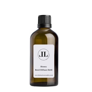 Könnte beinhalten: Eine braune Glasflasche mit schwarzem Deckel und einem weißen Etikett. Das Etikett enthält einen schwarzen Kreis mit den Buchstaben "JL" darin. Der Text auf dem Etikett lautet "Honey Reed Diffuser Refill" und "www.lindsaylucascandles.co.uk".