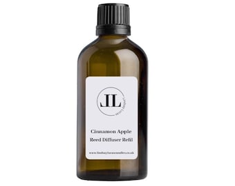 Op de afbeelding: Een bruine glazen fles met een zwarte dop en een wit etiket. Het etiket heeft een zwarte cirkel met de letters "JL" erin. De tekst op het etiket luidt "Cinnamon Apple Reed Diffuser Refill" en "www.lindsaylucascandles.co.uk".