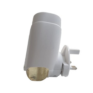 May include: A white plug-in air freshener with a gold-coloured, rounded bottom. The air freshener has a cylindrical top and a three-pin plug. The design is simple and modern, suitable for home fragrance.