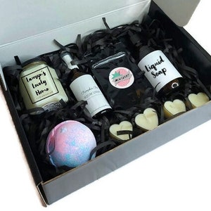 May include: A black gift box filled with bath and body products. The box contains a candle, bath bomb, liquid soap, and room spray. The candle is labeled "Tawnya's Lovely Home".