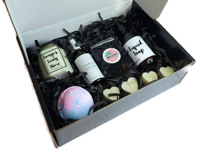 May include: A black gift box filled with bath and body products. The box contains a candle, bath bomb, liquid soap, and room spray. The candle is labeled "Tawnya's Lovely Home".