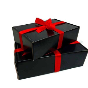 May include: Two black gift boxes tied with a red ribbon. The boxes are stacked on top of each other.