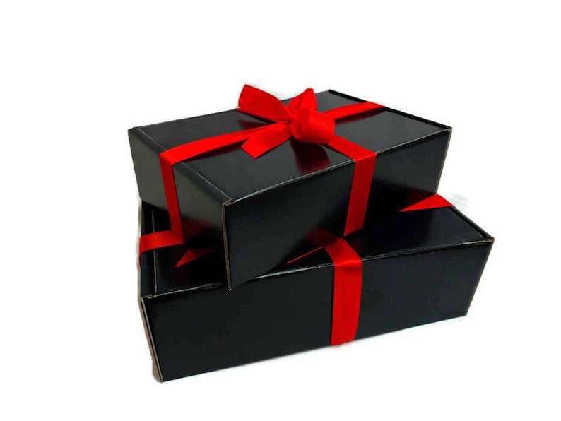 May include: Two black gift boxes tied with a red ribbon. The boxes are stacked on top of each other.