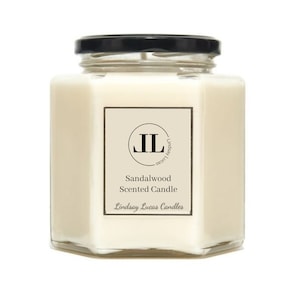 May include: A hexagonal glass jar candle with a black lid. The candle is white and has a label that says "Sandalwood Scented Candle" and "Lindsay Lucas Candles". The label also has a logo with the initials "JL" in a circle.