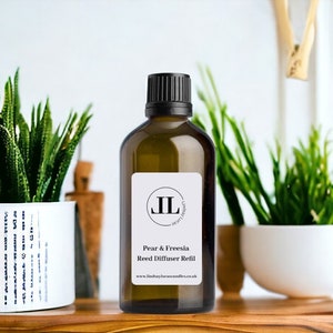 Puede incluir: Una botella de vidrio marr&oacute;n con una tapa negra y una etiqueta blanca. La etiqueta tiene un logotipo negro con las letras "JL" y el texto "Pear & Freesia Reed Diffuser Refill" y "www.lindsaylaurencandles.co.uk".