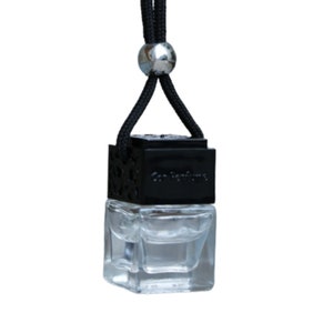 May include: Black car air freshener with a clear glass bottle and a black string with a silver bead. The bottle has a black cap with the text "Car Perfume" on it.