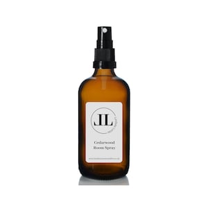 May include: A brown glass bottle with a black spray nozzle. The bottle has a white label with the text "Cedarwood Room Spray" and a website address. The label also features a black circle with the initials "IL" inside.