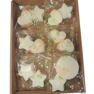 May include: A cardboard box containing individually wrapped soaps in star, heart, and round shapes. The white soaps are decorated with peach and green floral designs. Each soap is packaged in clear plastic with a floral pattern.