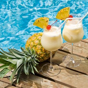 May include: Two glasses of pineapple cocktails with a pineapple garnish and a cherry on top, sitting on a wooden surface next to a pineapple.
