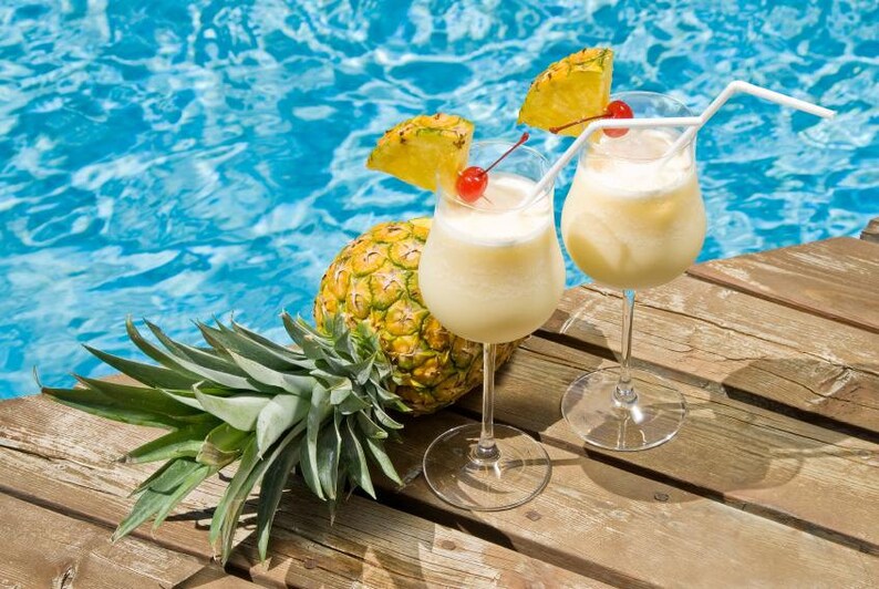 May include: Two glasses of pineapple cocktails with a pineapple garnish and a cherry on top, sitting on a wooden surface next to a pineapple.