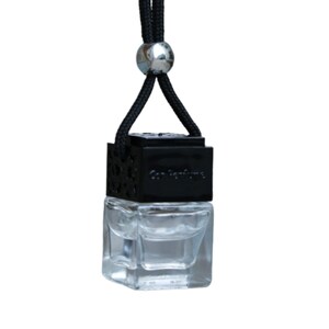 May include: Black car air freshener with a clear glass bottle and a black string with a silver bead. The bottle has a black cap with the text "Car Perfume" on it.