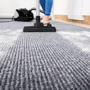 Puede incluir: Una persona aspirando una alfombra gris con una aspiradora negra. La alfombra tiene polvo o suciedad blanca.