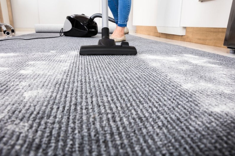 Puede incluir: Una persona aspirando una alfombra gris con una aspiradora negra. La alfombra tiene polvo o suciedad blanca.