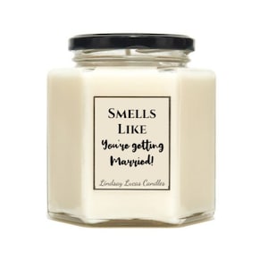May include: A cream-coloured candle in a hexagonal glass jar with a black lid. The label reads "Smells Like You're getting Married!" with the brand name "Lindsay Lucas Candles" below. A wedding-themed gift.