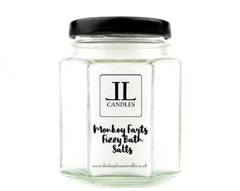 May include: A glass jar with a black lid filled with white bath salts. The label reads "Monkey Farts Fizzy Bath Salts" and "JL Candles" with the website address "www.lindsayjacascandles.co.uk".