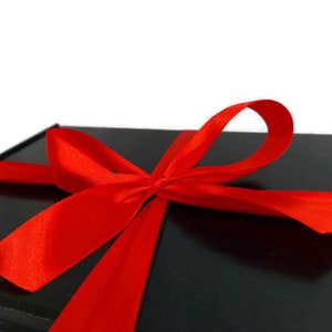 May include: A black gift box with a large red satin bow. The bow is tied in a knot with the ends of the ribbon flowing down the sides of the box.