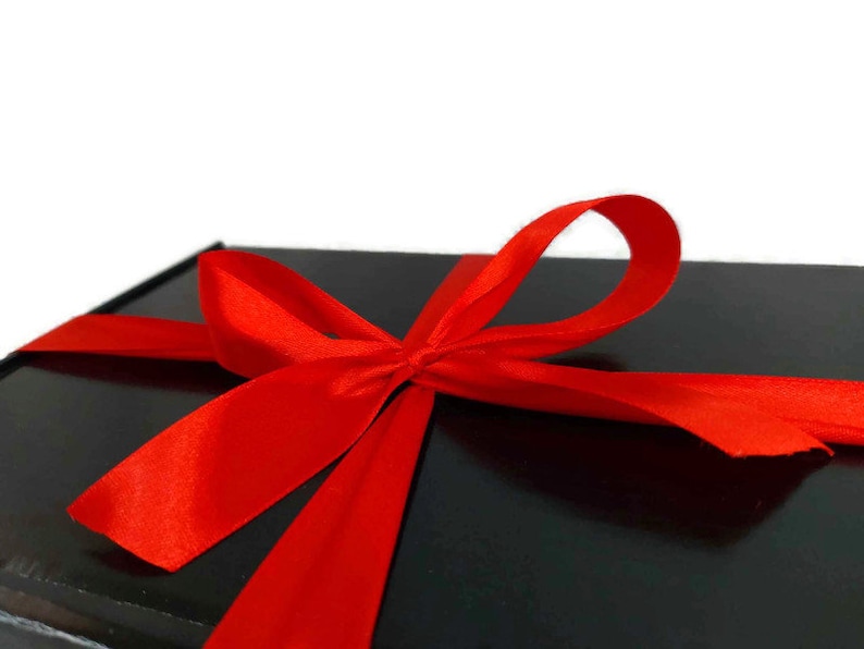 May include: A black gift box with a large red satin bow. The bow is tied in a knot with the ends of the ribbon flowing down the sides of the box.