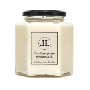 May include: A hexagonal glass jar candle with a black lid. The candle is white and has a label that says "Black Pomegranate Scented Candle" and "Lindsay Lucas Candles".