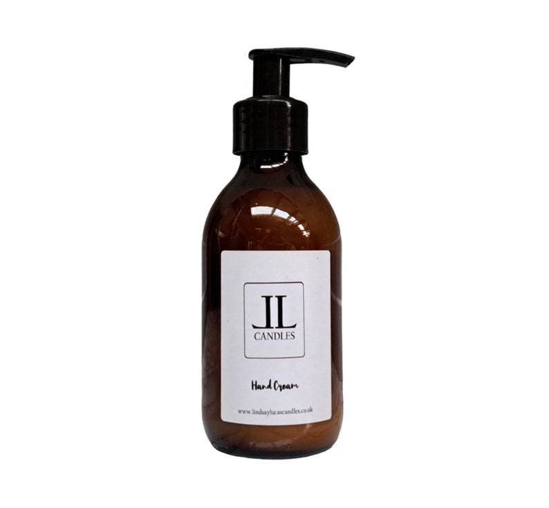 May include: A brown glass bottle with a black pump dispenser filled with hand cream. The bottle has a white label with the text "JL Candles" and "Hand Cream" printed on it. The website address "www.lindaylascandles.co.uk" is printed at the bottom of the label.