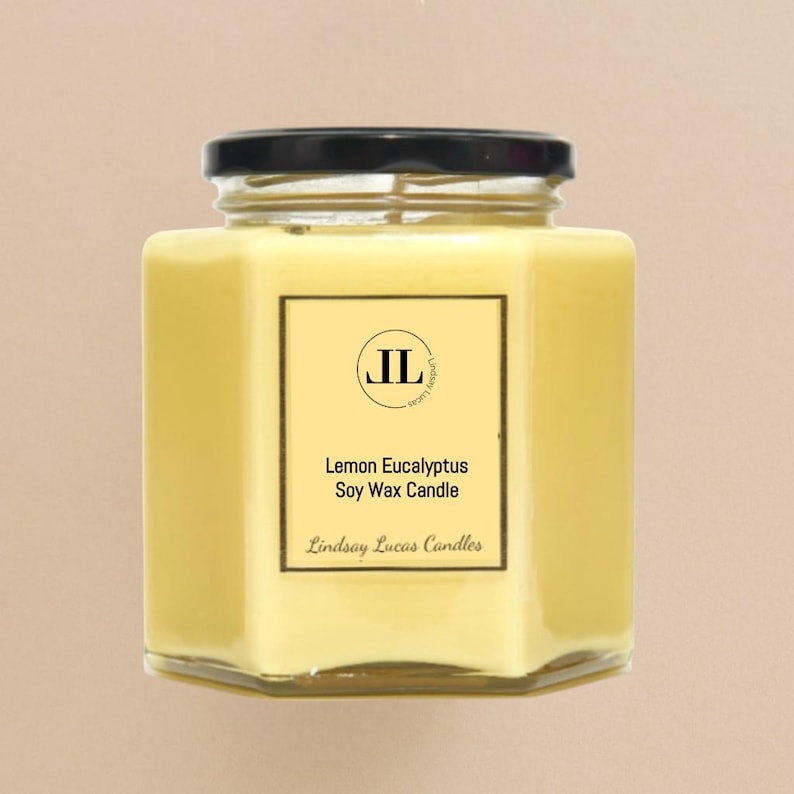 May include: A hexagonal glass jar candle with a black lid. The candle is filled with yellow wax and has a label that reads "Lemon Eucalyptus Soy Wax Candle" with the brand name "Lindsay Lucas Candles".