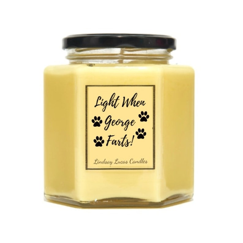 May include: A yellow hexagonal glass candle jar with a black lid. The label reads "Light When George Farts!" with paw prints and the text "Lindsay Lucas Candles".