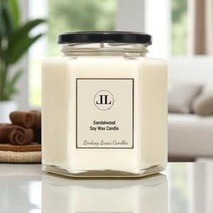 May include: A clear, hexagonal glass jar candle with a black lid. The candle has a white wax fill and a rectangular label with the text "Sandalwood Soy Wax Candle" and the brand name "Lindsay Lucas Candles".
