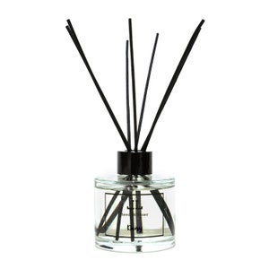 May include: A clear glass bottle with a black lid and black reeds, filled with a clear liquid. The bottle has a label that reads "Reed Diffuser" and "Daisy".