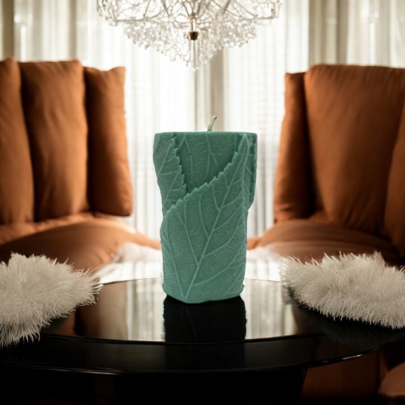 May include: A teal green candle with a leaf design sits on a black table in front of two brown couches.