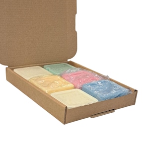 May include: A brown cardboard box holding eight square soaps in pastel shades. The soaps are individually wrapped in clear plastic. Colours include yellow, pink, blue, green, and cream.