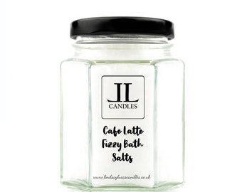 May include: A glass jar with a black lid filled with white bath salts. The jar has a label that says "Cafe Latte Fizzy Bath Salts" and "IL Candles" with the website address "www.lindsayslucascandles.co.uk".