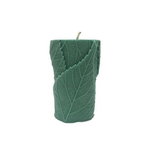 May include: A green pillar candle with a leaf design. The candle is made of wax and has a natural, earthy look.