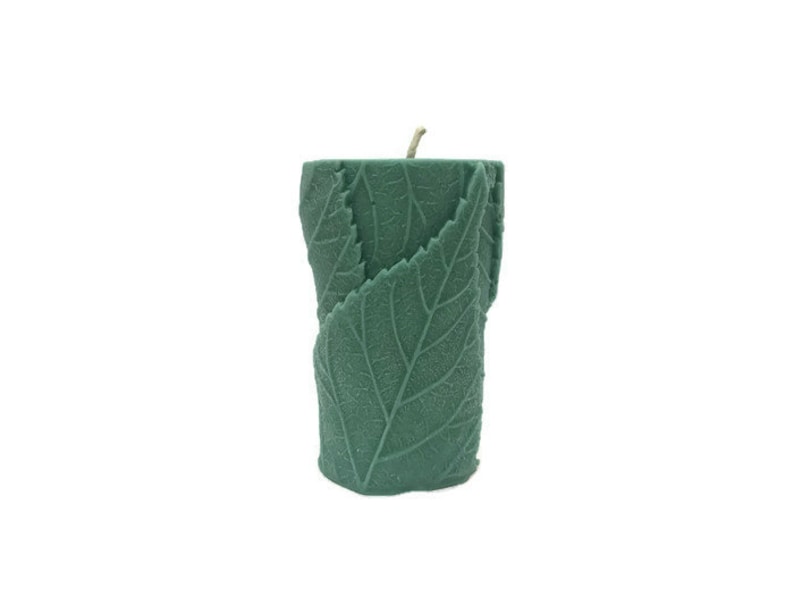 May include: A green pillar candle with a leaf design. The candle is made of wax and has a natural, earthy look.