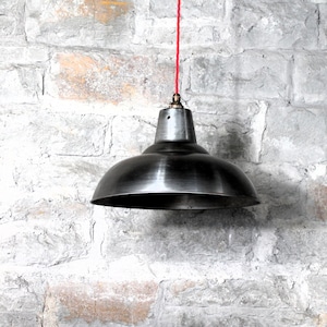 Könnte beinhalten: Eine schwarze Metall-Pendelleuchte mit einem roten Kabel, das an einer Backsteinwand hängt.