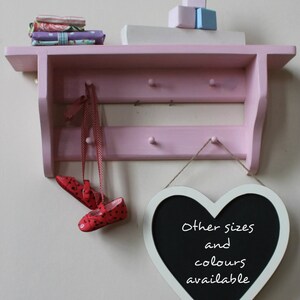 Peut inclure: Une étagère en bois rose avec deux étagères et des crochets, décorée de chutes de tissu et d'une pancarte en forme de cœur en ardoise qui indique "Autres tailles et couleurs disponibles".