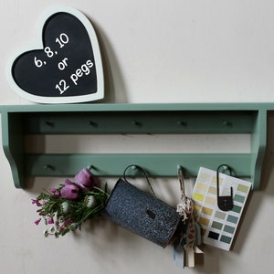 Puede incluir: Una estantería de madera verde con clavijas, que sostiene una pizarra en forma de corazón con el texto "6, 8, 10 o 12 clavijas". Un recipiente de metal, flores y muestras de color cuelgan de las clavijas. La estantería está pintada de verde.