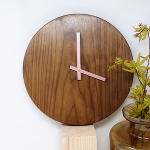 Op de afbeelding: Een ronde houten klok met roze leren wijzers. De klok is gemonteerd op een houten standaard.