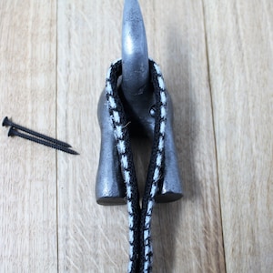 May include: A black and white striped rope is looped around a silver metal hook. The hook is mounted on a wooden surface.