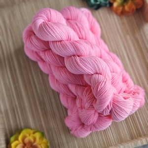 May include: A skein of bright pink yarn with a twisted texture, featuring a vibrant solid color. The yarn is composed of multiple strands wound together, creating a soft and uniform appearance throughout the entire length of the fiber bundle.