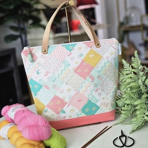 May include: A patchwork tote bag with a pink base and leather handles. The bag features a variety of pastel-colored fabric squares with horse and boot patterns. Knitting needles, yarn, and scissors are next to the bag.