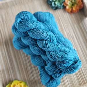 May include: A vibrant teal blue yarn skein with a twisted texture. The yarn is presented as a single, continuous bundle of fiber, showcasing a deep, saturated color and a smooth, matte finish throughout the entire length of the twisted strands.