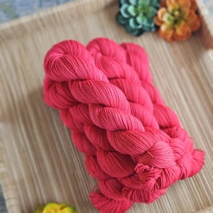 May include: A vibrant hot pink yarn skein twisted into a thick, textured bundle. The yarn features a consistent, saturated magenta hue with visible fiber strands throughout the twist, showcasing a soft, matte finish and a dense, coiled structure.
