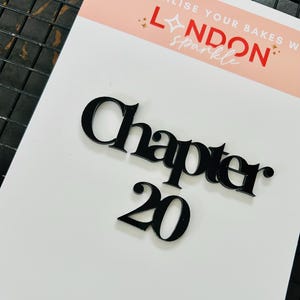 May include: A black acrylic cake topper with the words "Chapter 20" on a white background. The topper is designed with a modern font and is suitable for a 20th birthday celebration. The background has the text "LONDON sparkle".