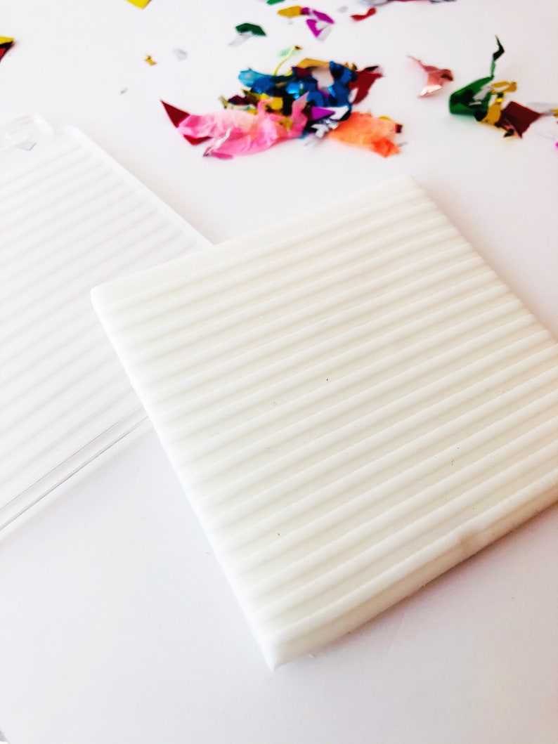 Puede incluir: Dos cuadrados blancos texturados, uno con una superficie lisa y el otro con l&iacute;neas en relieve. Los cuadrados est&aacute;n sobre una superficie blanca.
