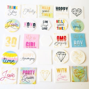 Puede incluir: Una colecci&oacute;n de 20 adornos para pasteles redondos y cuadrados con varios dise&ntilde;os y textos. Los adornos presentan una variedad de colores, incluyendo rosa, azul, amarillo, verde, rojo y blanco. Algunos de los textos en los adornos incluyen "Feliz cumplea&ntilde;os", "Amor", "Reina de la fiesta", "Es una ni&ntilde;a", "Es un ni&ntilde;o", "Gracias", "Hola buenos tiempos", "Vive R&iacute;e Ama", "OMG &iexcl;Felicidades!" y "Sr. y Sra.".