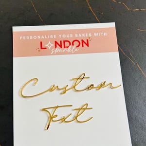 Pode incluir: Um cartão branco com texto dourado em itálico que diz "Custom Text". O cartão também apresenta o texto "Personalise Your Bakes With London Sparkle" num esquema de cores rosa e vermelho.