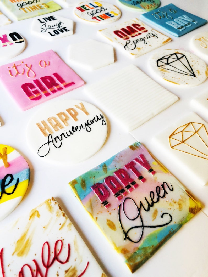 Puede incluir: Surtido de adornos para pasteles redondos y cuadrados con varios colores y dise&ntilde;os. Los adornos incluyen texto como "Live Laugh Love", "Hello Good Times", "It's a Girl", "Happy Anniversary" y "Party Queen".