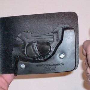 May include: A black holster with a molded gun shape and a blue handgun. The holster has the text "XWANGCONCEALMENT.COM RUGER LCR PATENTED". The handgun is held in a hand.
