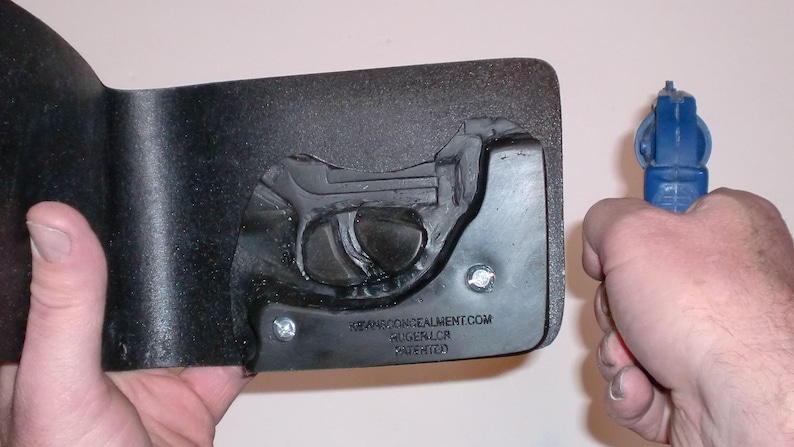 May include: A black holster with a molded gun shape and a blue handgun. The holster has the text "XWANGCONCEALMENT.COM RUGER LCR PATENTED". The handgun is held in a hand.
